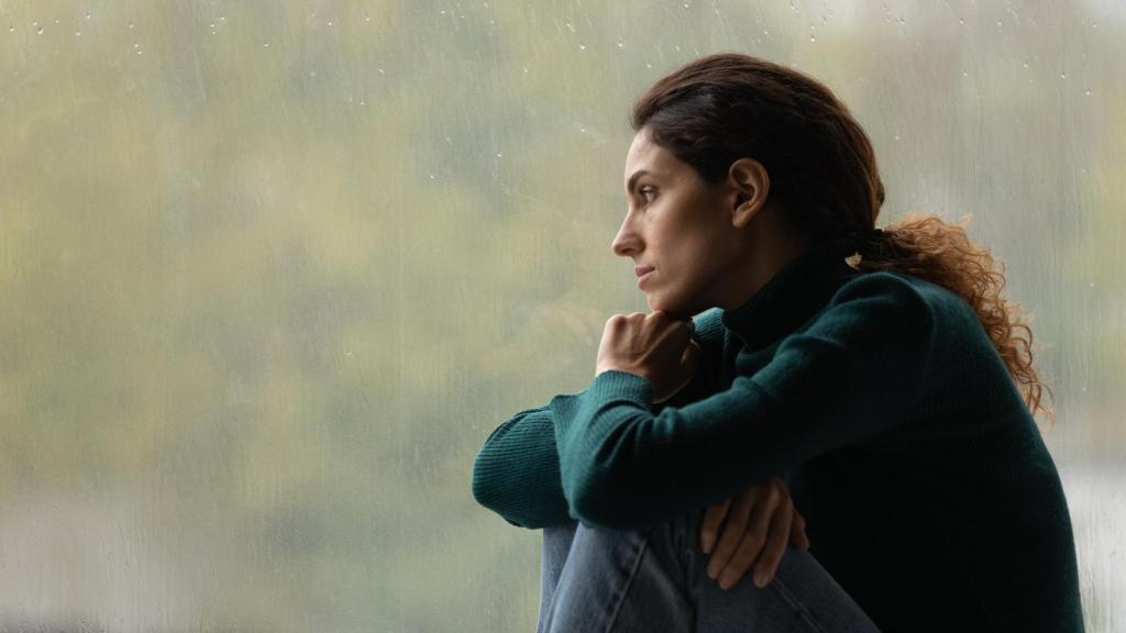 Imagen de una mujer desanimada mirando por la ventana.