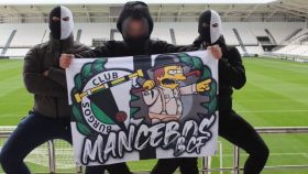 Tres ultras con una bandera del grupo Mancebos BCF.