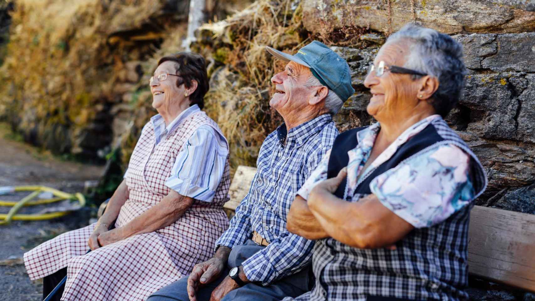 Tres paisanos gallegos descansando y conversando en un banco.