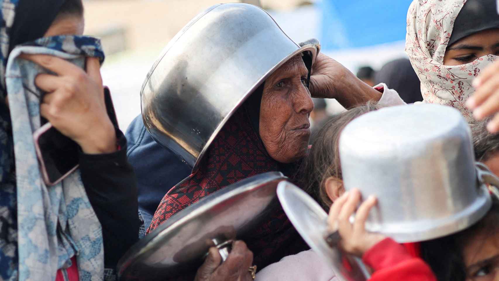 Una anciana esperan para recibir comida con una olla en la cabeza, este miércoles.