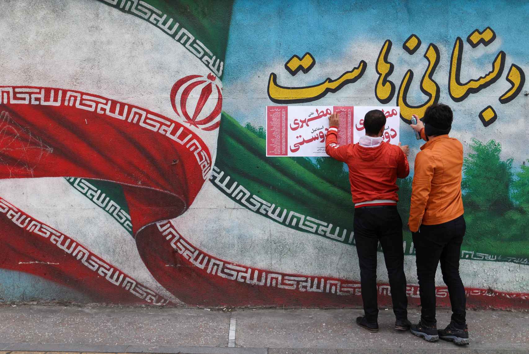 Dos hombres ponen carteles de campaña en Teherán.