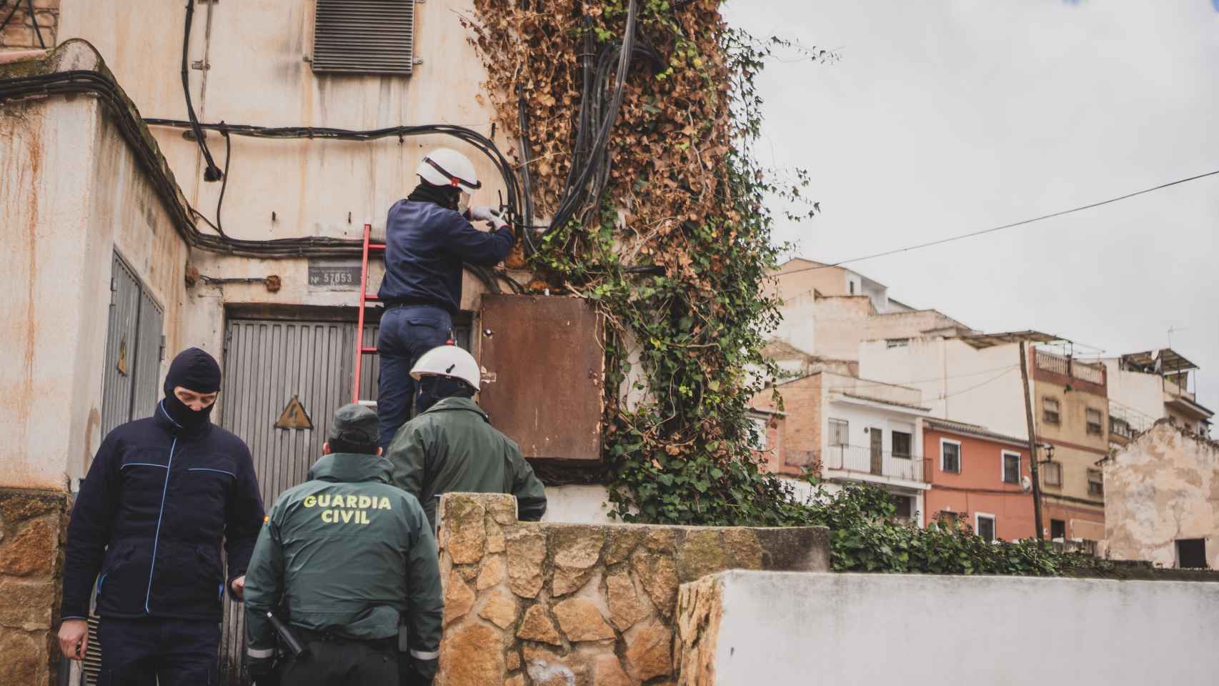 Técnicos de Endesa cubiertos con pasamontañas desinstalan cables que captan luz ilegal acompañados por la Guardia Civil.