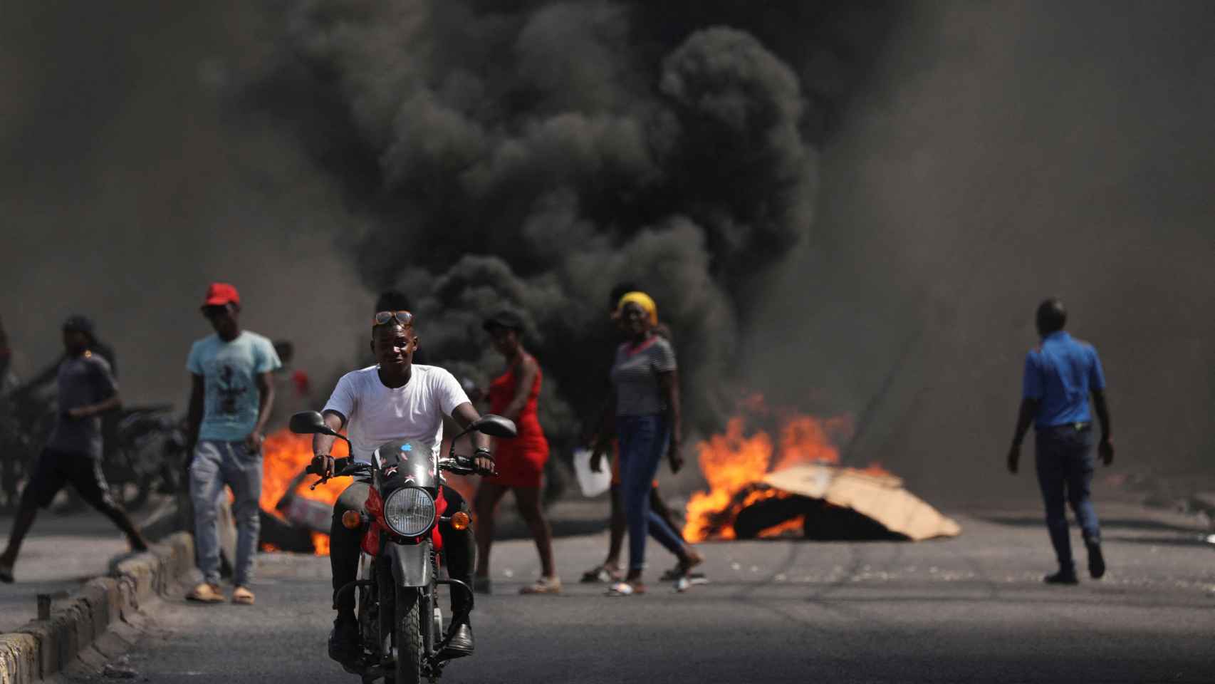 Un hombre se desplaza en moto entre las llamas originadas por los disturbios