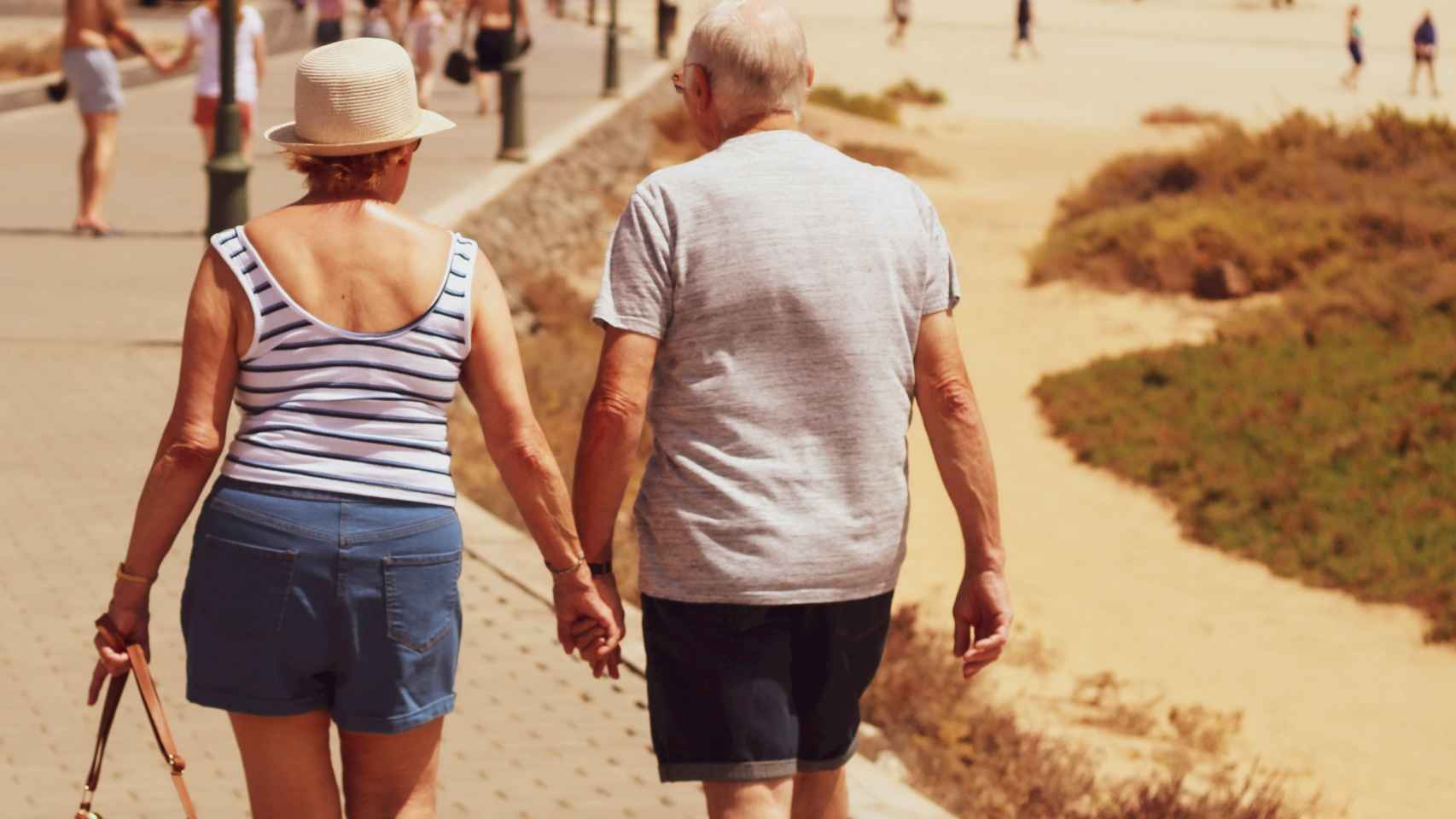 Una pareja de jubilados camina por un paseo marítimo.