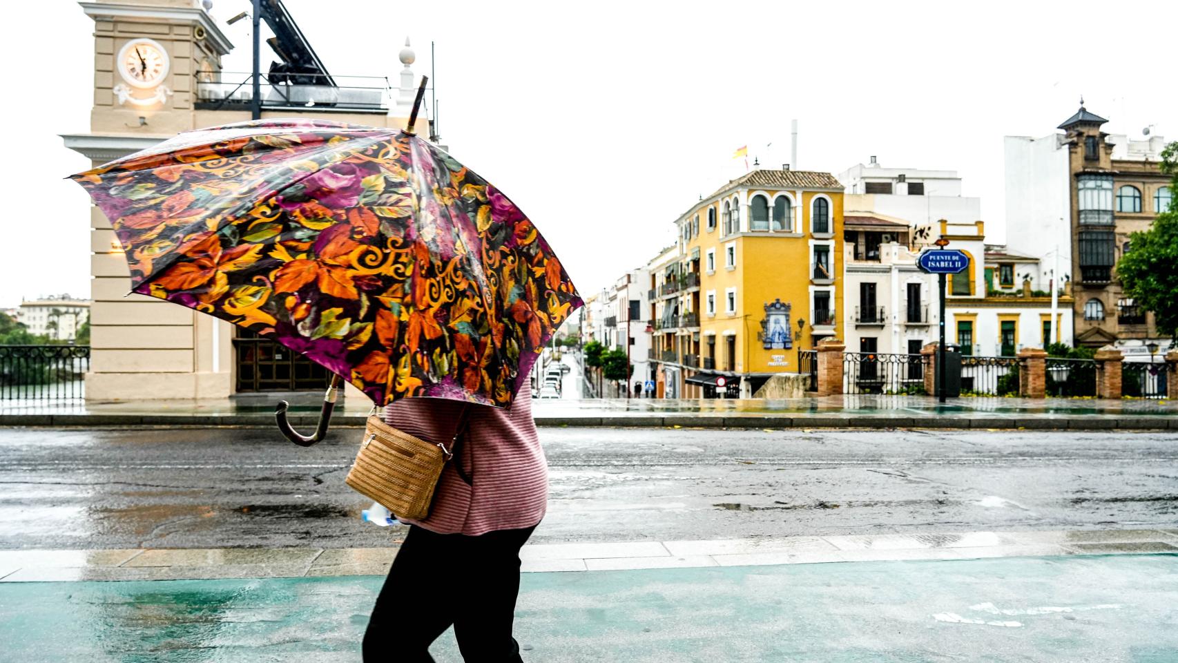 Una mujer con dificultades para protegerse de la lluvia en el Puente de Triana.