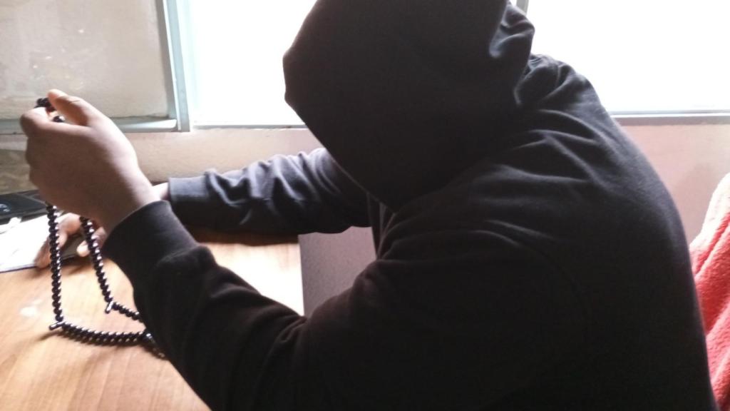 Mame, sujetando un rosario, junto a la ventana del humilde piso que comparte con unos compatriotas de Senegal.