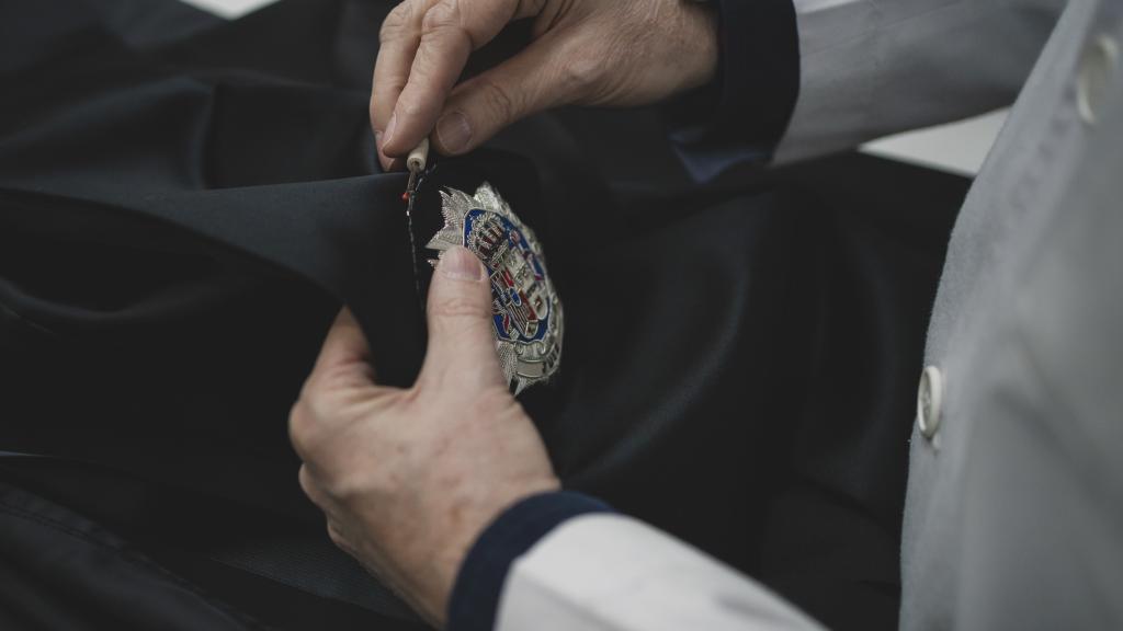 Un empleado de la sastrería descose una insignia de una toga.