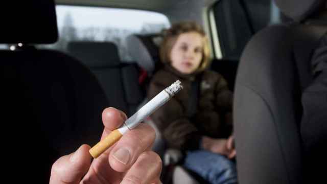 Imagen de una persona fumando en el interior del coche en el que también va un niño