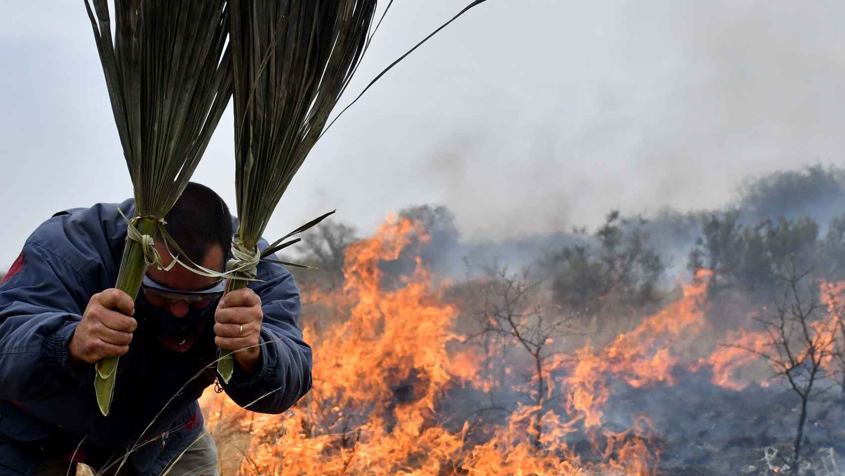Un hombre intenta extinguir las llamas con hojas de palma durante un incendio en la parte norte de la provincia de Córdoba.