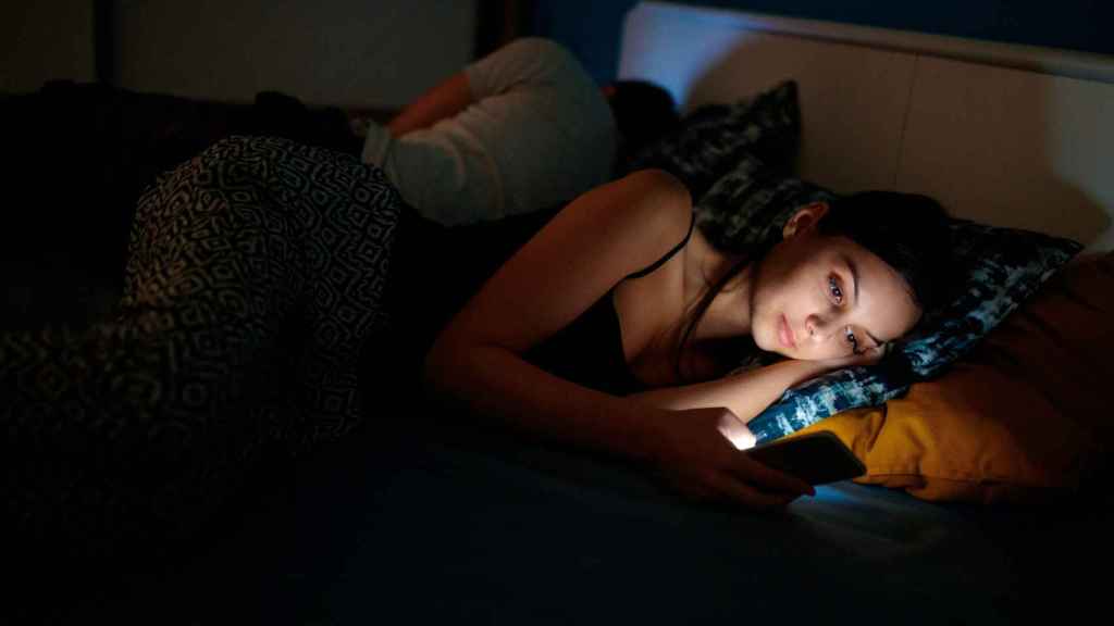Una mujer con insomnio viendo el teléfono móvil en la cama.