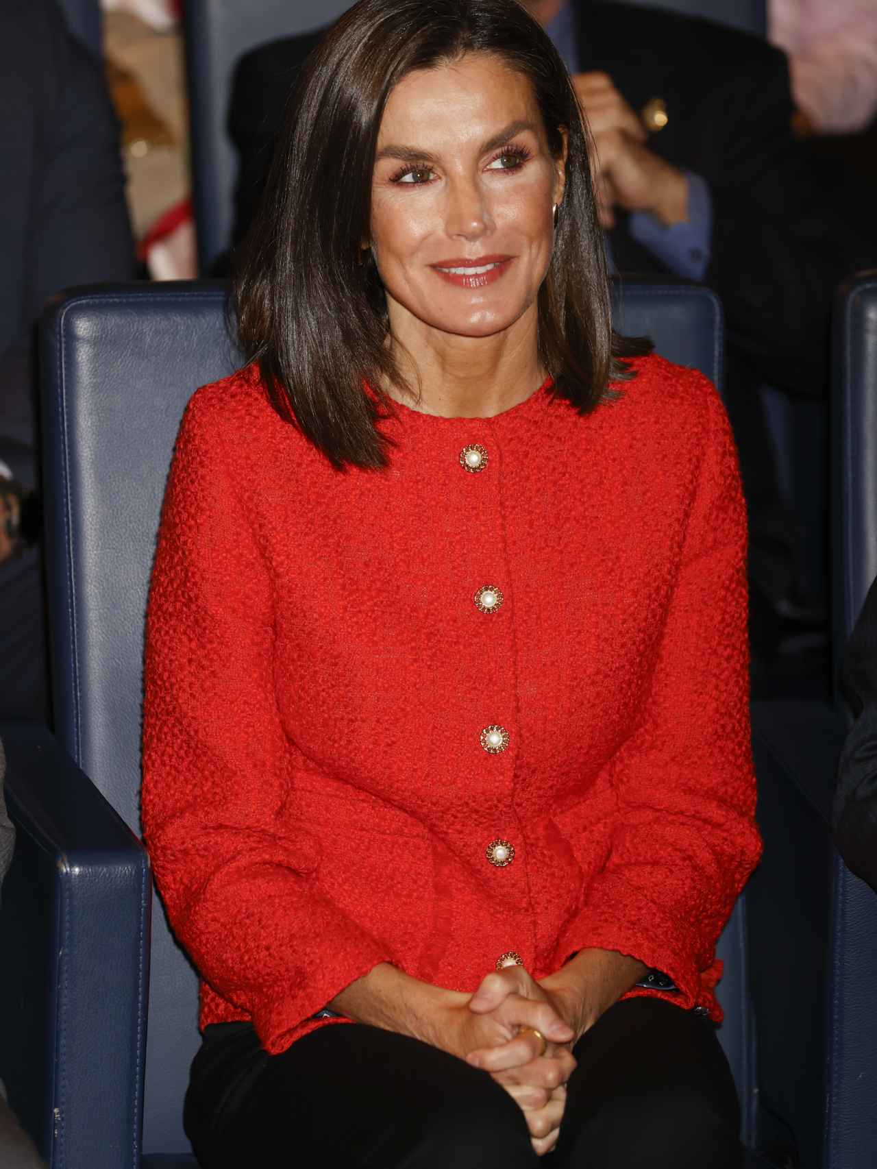 Letizia Ortiz con una chaqueta en tweed rojo sentada disfrutando del acto.