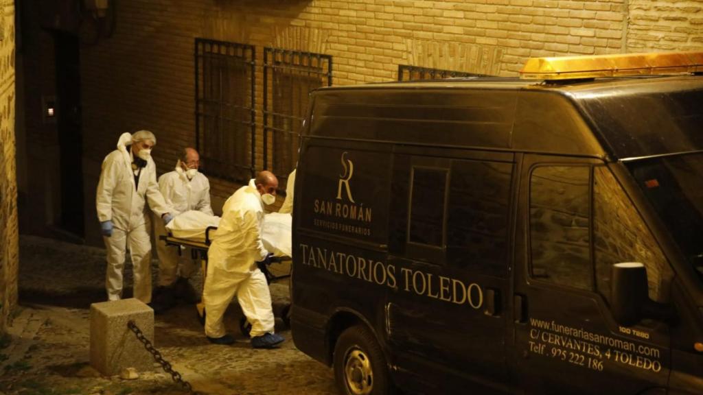 Los servicios funerarios sacan a uno de los cadáveres de la vivienda.