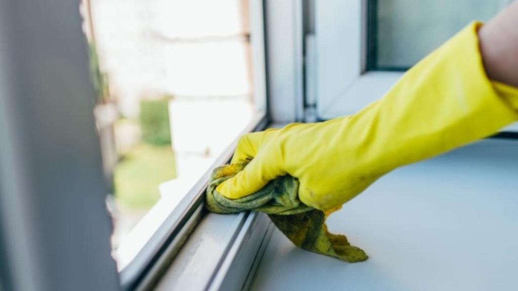 Una persona limpiando los rieles de una ventana.