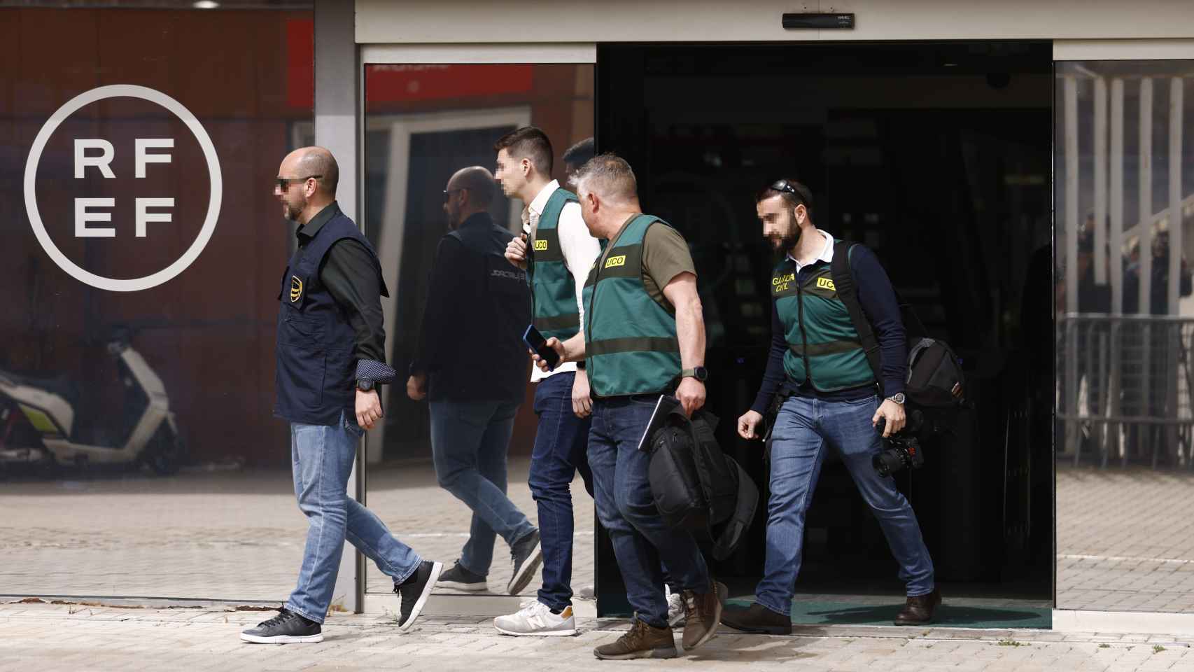 Un agente de la Europol y varios agentes de la Unidad Central Operativa (UCO) de la Guardia Civil salen de la Real Federación Española de Fútbol