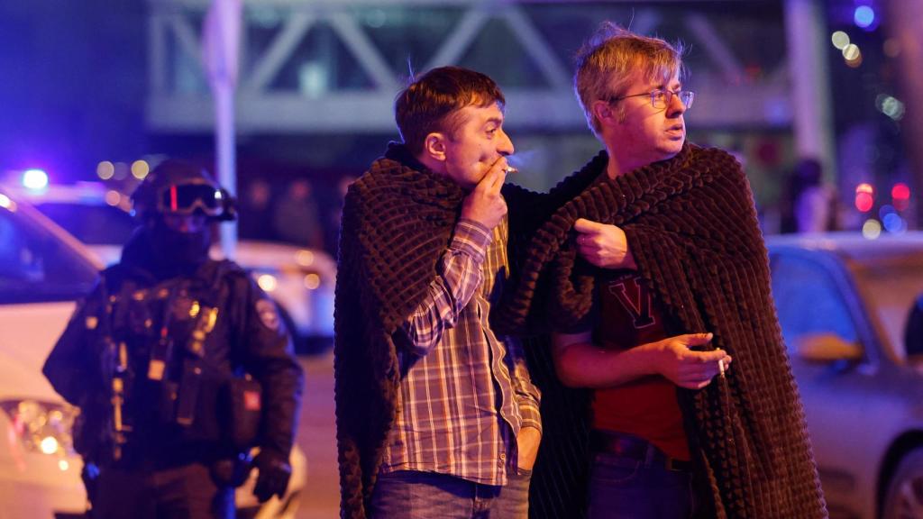 Varios hombres se cubren con mantas fuera de la sala de conciertos Crocus City Hall.