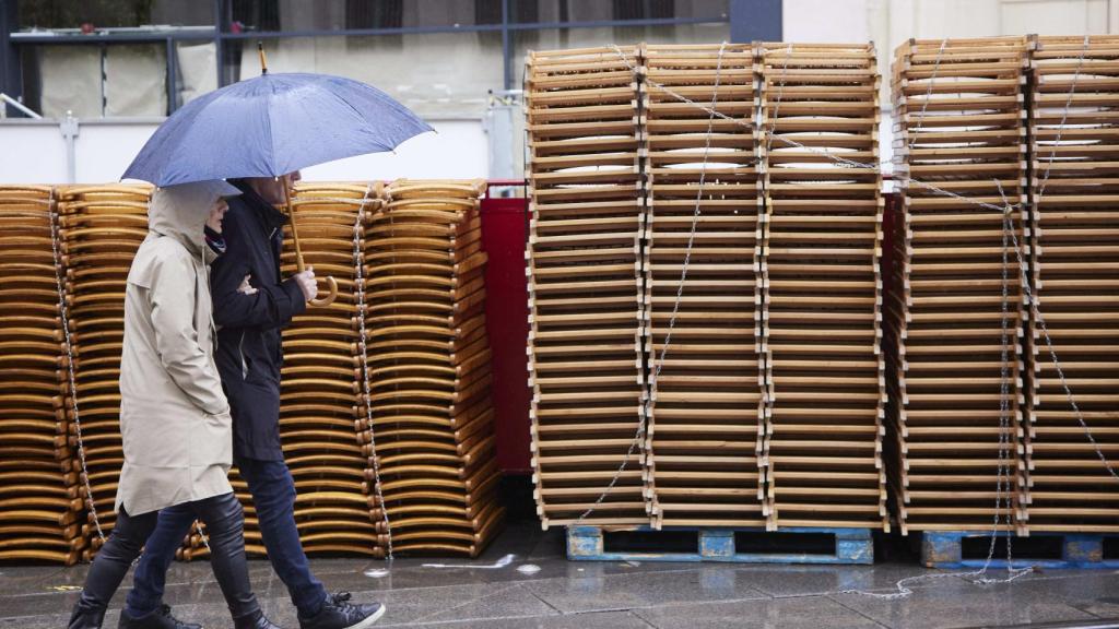 Una pareja pasea bajo la lluvia por la Avenida de la Constitución con las sillas retiradas.