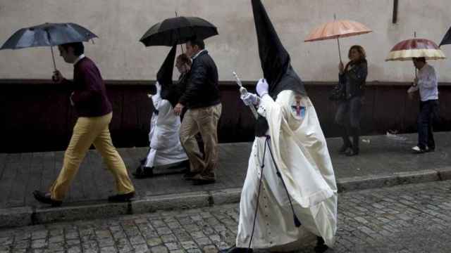 Un nazareno acude a una procesión mientras cae la lluvia.
