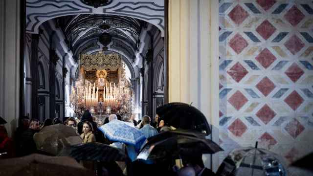 Un grupo de personas con paraguas observando una imagen de Semana Santa en Málaga.