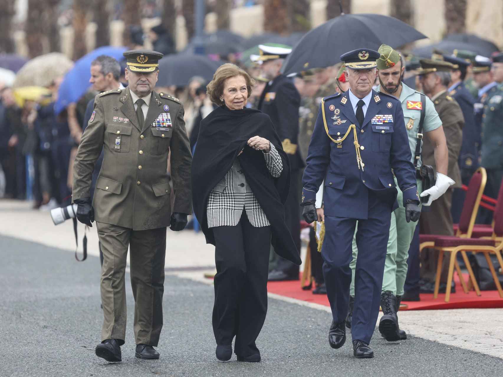 La reina Sofía camina con autoridades militares mientas la lluvia da un pequeño respiro.