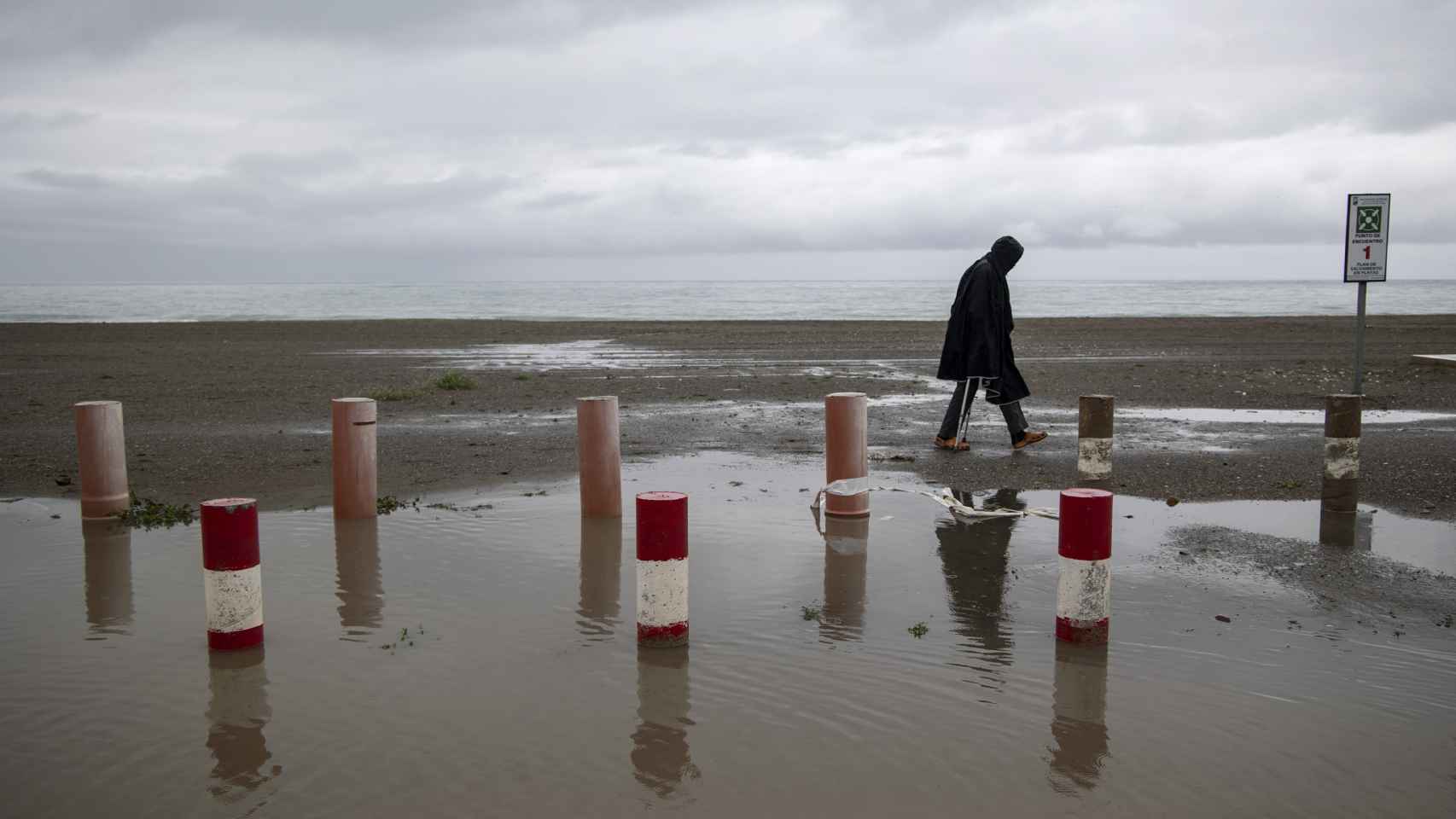 Una persona camina por la playa de Los Álamos en Torremolinos, bajo la lluvia que está cayendo en la provincia de Málaga este domingo.