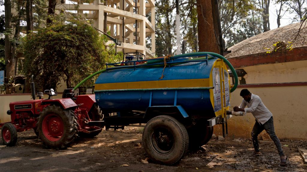 Un conductor cierra el grifo de un camión cisterna tras llenarlo con agua potable para suministrar agua en un barrio.