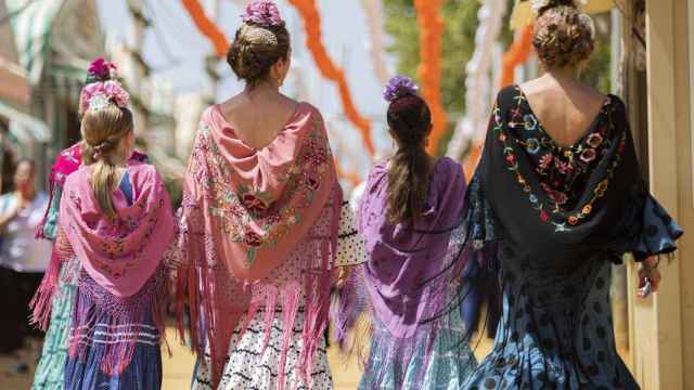 Cuatro mujeres vestidas de flamenca pasean por el Real de la Feria de Abril.