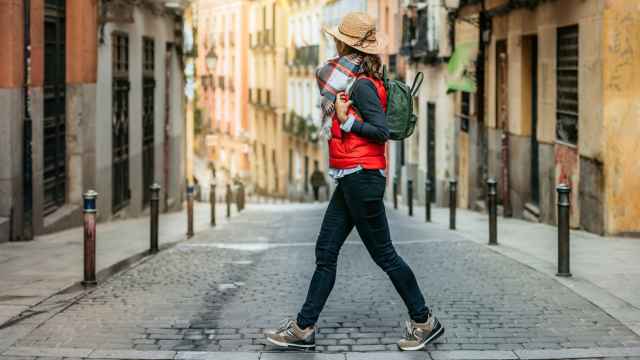 Una mujer turista con gorra y mochila, cruza una calle en el centro histórico de una ciudad española.