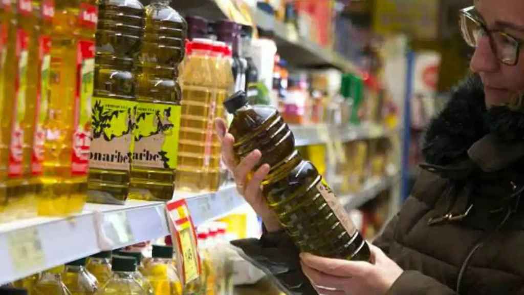 Una mujer cogiendo una botella de aceite en un supermercado.