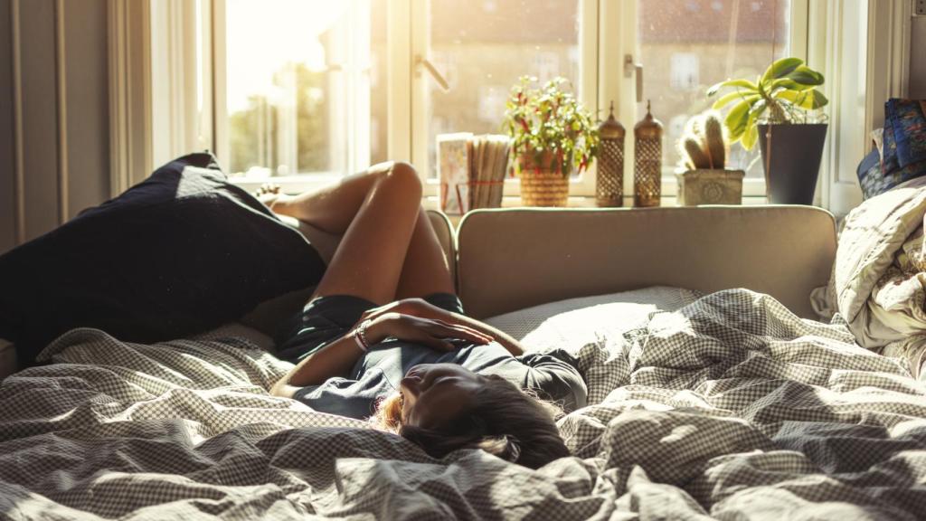 Una mujer descansa en su cama junto a varias plantas.