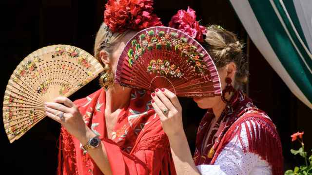 Dos mujeres vestidas de flamenca se protegen del sol en la Feria.