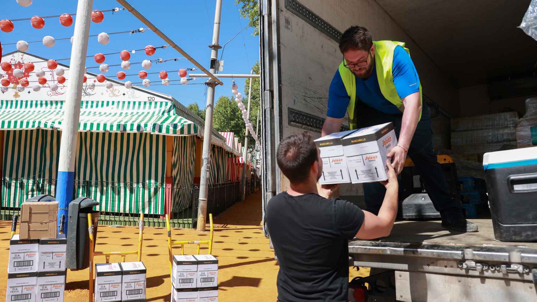 Operarios transportan cajas de manzanilla en el Real de la Feria.