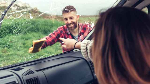 Un hombre limpia el parabrisas de su coche mientras una mujer señala la mancha.