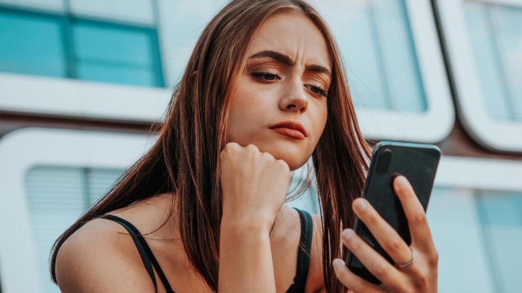 Mujer joven mirando el móvil con desconfianza.