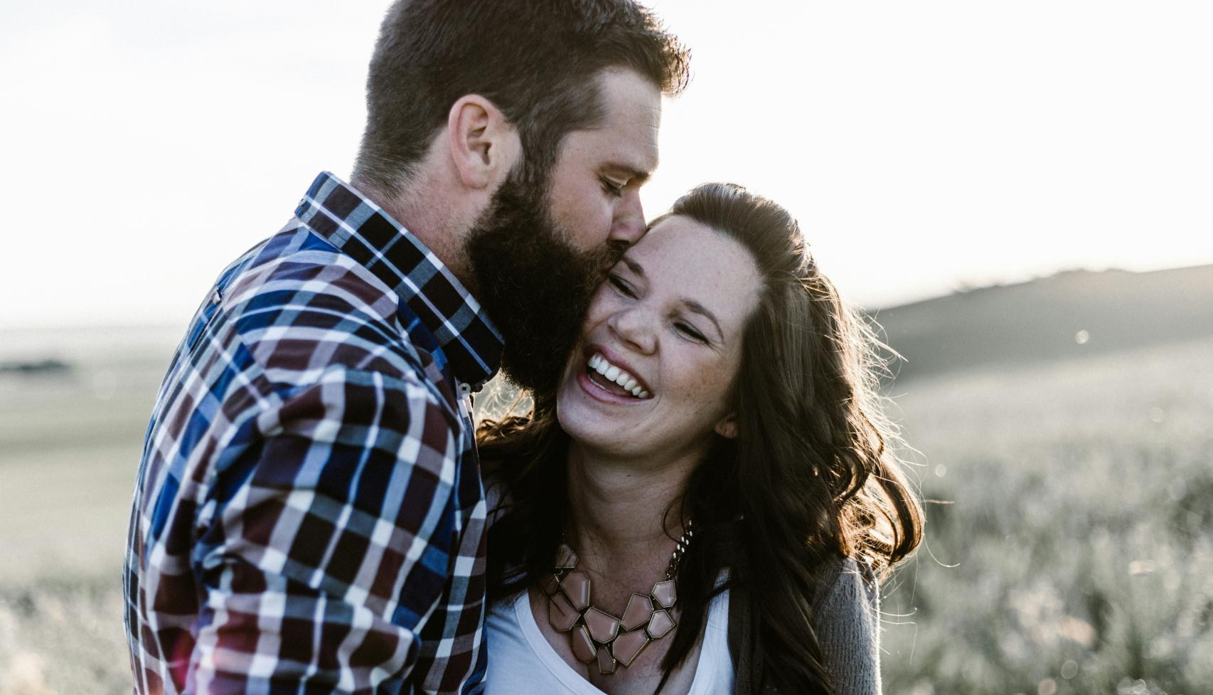 Hombre besando a una mujer sonriendo.