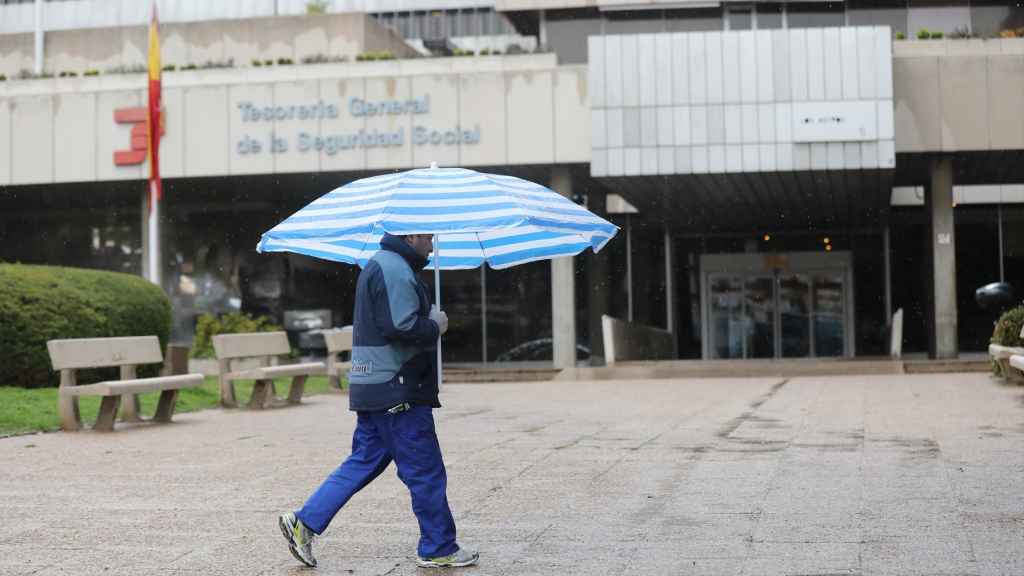 Un hombre con paraguas pasa frente a una oficina de la Tesorería General de la Seguridad Social, en una imagen de archivo.