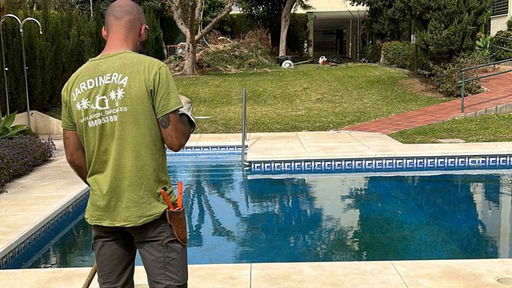 Un jardinero, trabajando frente a una piscina cerrada.