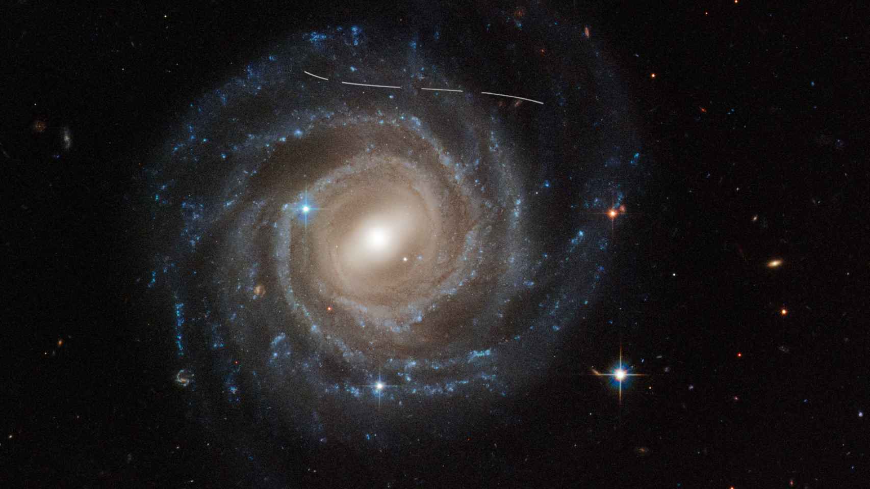 Fotografía de Hubble de la galaxia espiral barrada UGC 12158  con las estela blanca de un asteroide