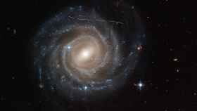 Fotografía de Hubble de la galaxia espiral barrada UGC 12158  con las estela blanca de un asteroide