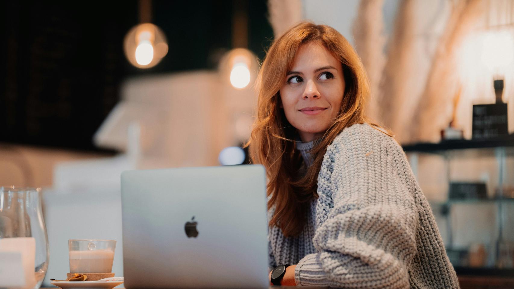 Mujer mirando de reojo con un portátil y un café.
