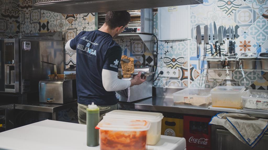 Maximiliano París en su puesto de mercado preparando una milanesa.