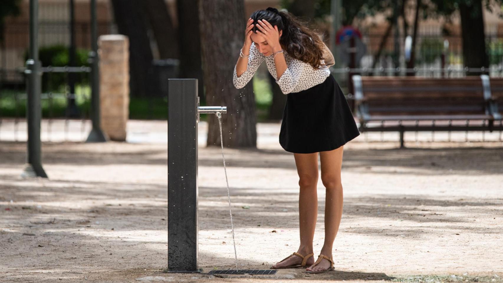 Una chica refrescándose en una fuente.