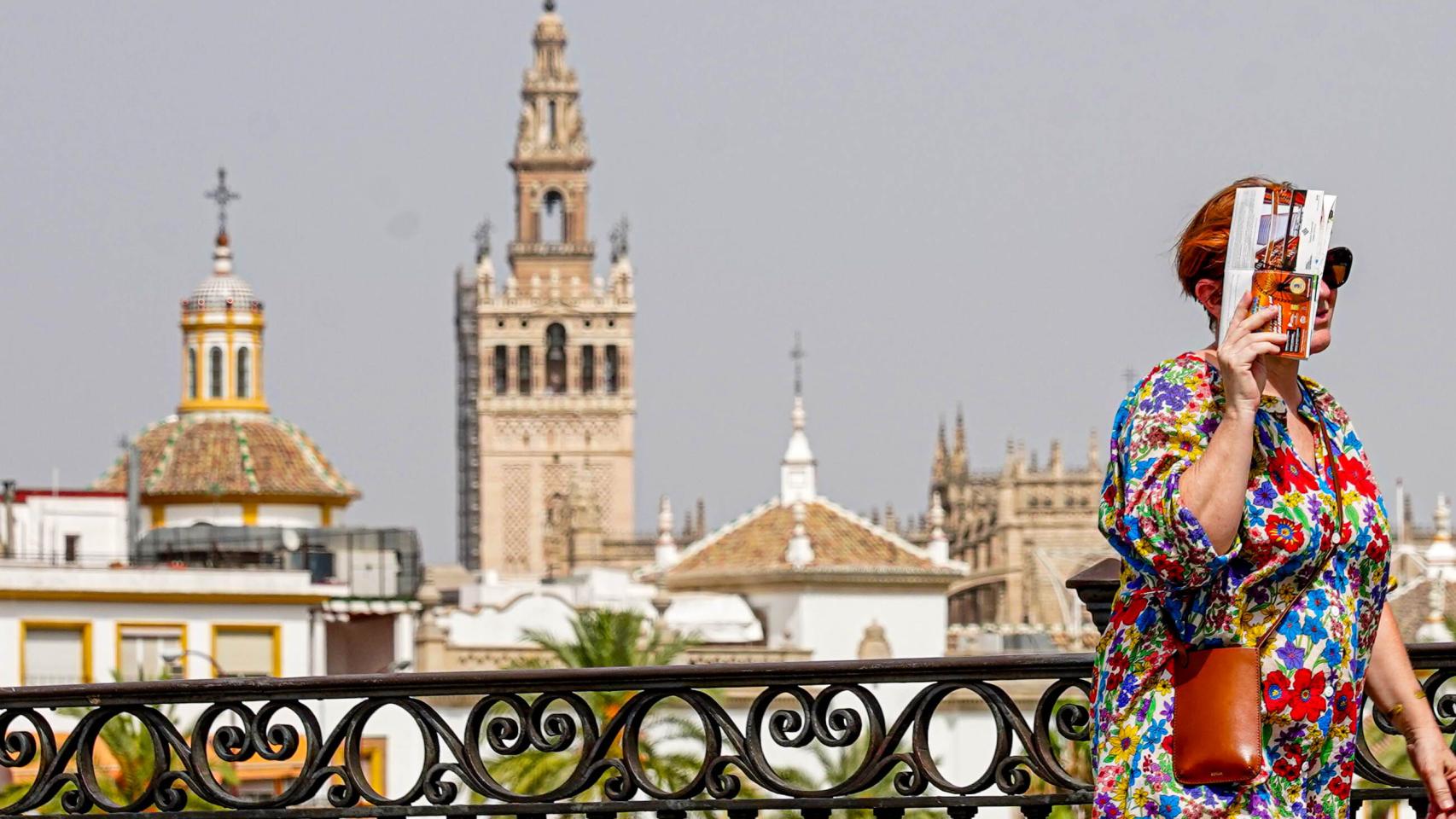 Una mujer se protege del calor mientras pasea por el Puente de Triana.