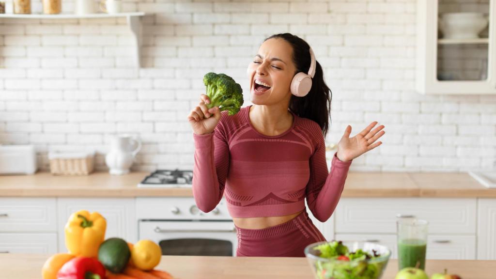 Mujer en la cocina cantando con un brócoli a modo de micrófono.