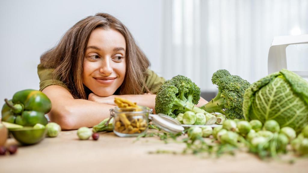 Mujer sobre la encima de la cocina mirando sonriente al brócoli.