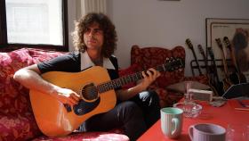 Sarria en el salón de su piso tocando la guitarra acústica