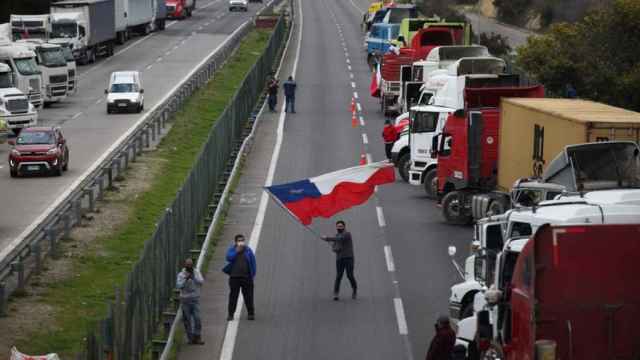 Un camionero agita la bandera chilena en medio del paro de camioneros y una carretera cortada.