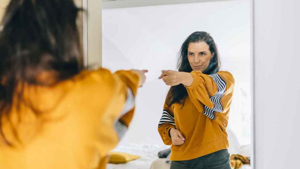 Mujer señalándose en el espejo, triunfante.