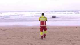 Un bombero observa el coche de la pareja palentina encallado a orillas de la playa de Oyambre.