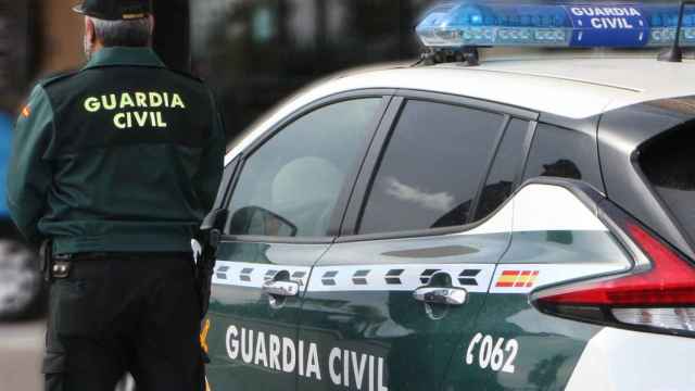 Un agente de la Guardia Civil, de espaldas, de pie junto a un vehículo oficial.