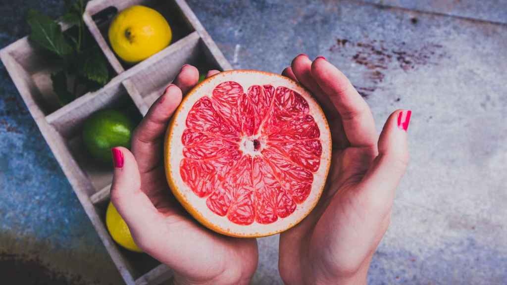 Manos sosteniendo la mitad de un pomelo.